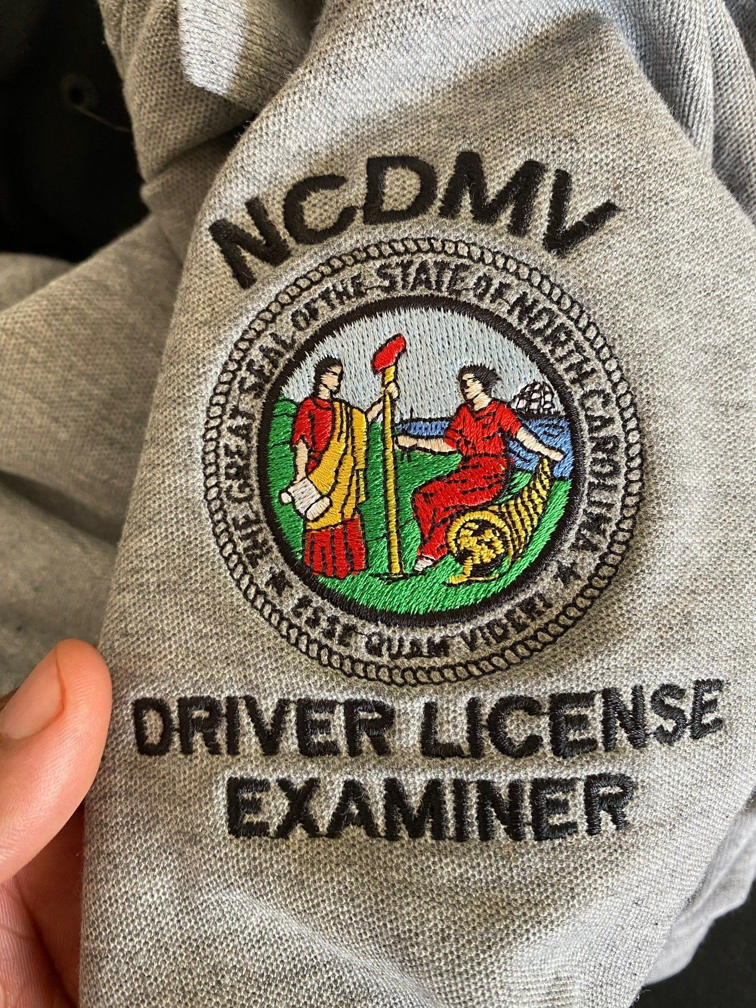 A person is holding a driver license examiner sweatshirt in their hand.