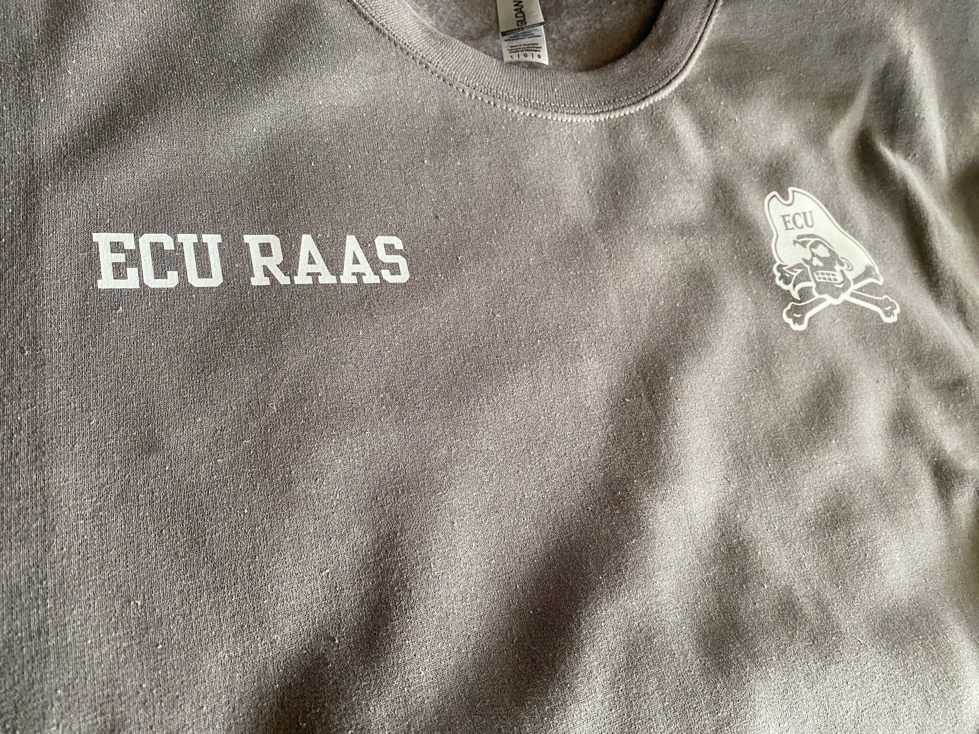 A close up of a grey shirt with the words ecu raas on it.
