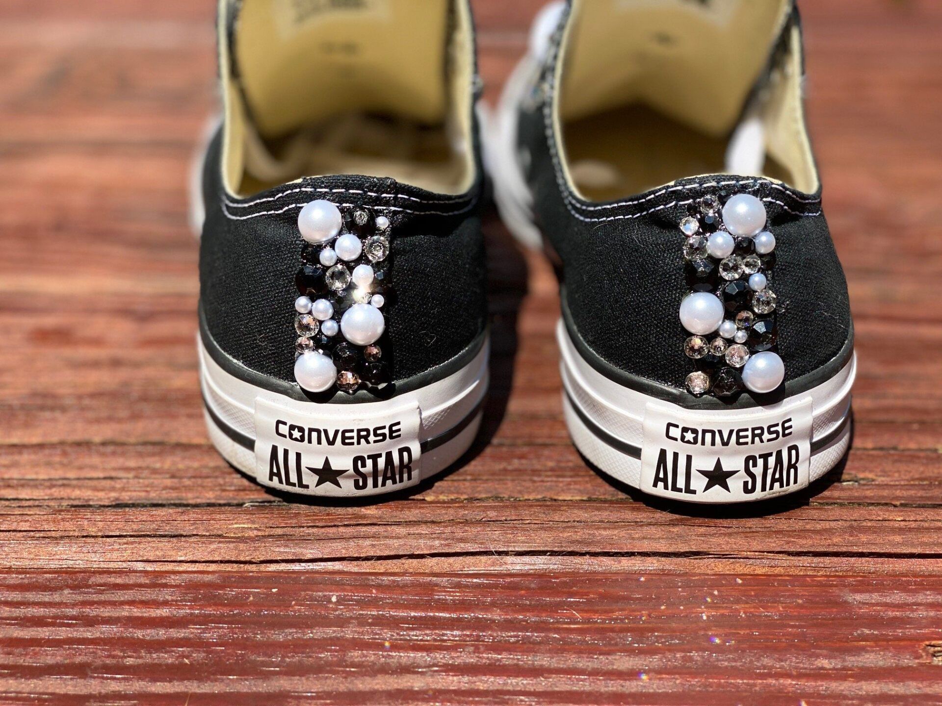 A pair of black converse shoes with pearls on them