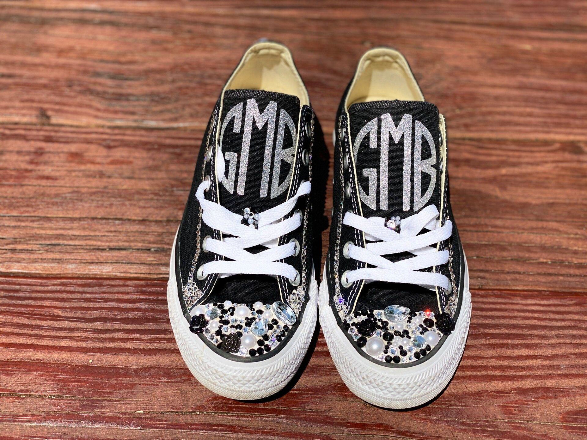 A pair of monogrammed converse shoes are sitting on a wooden table.