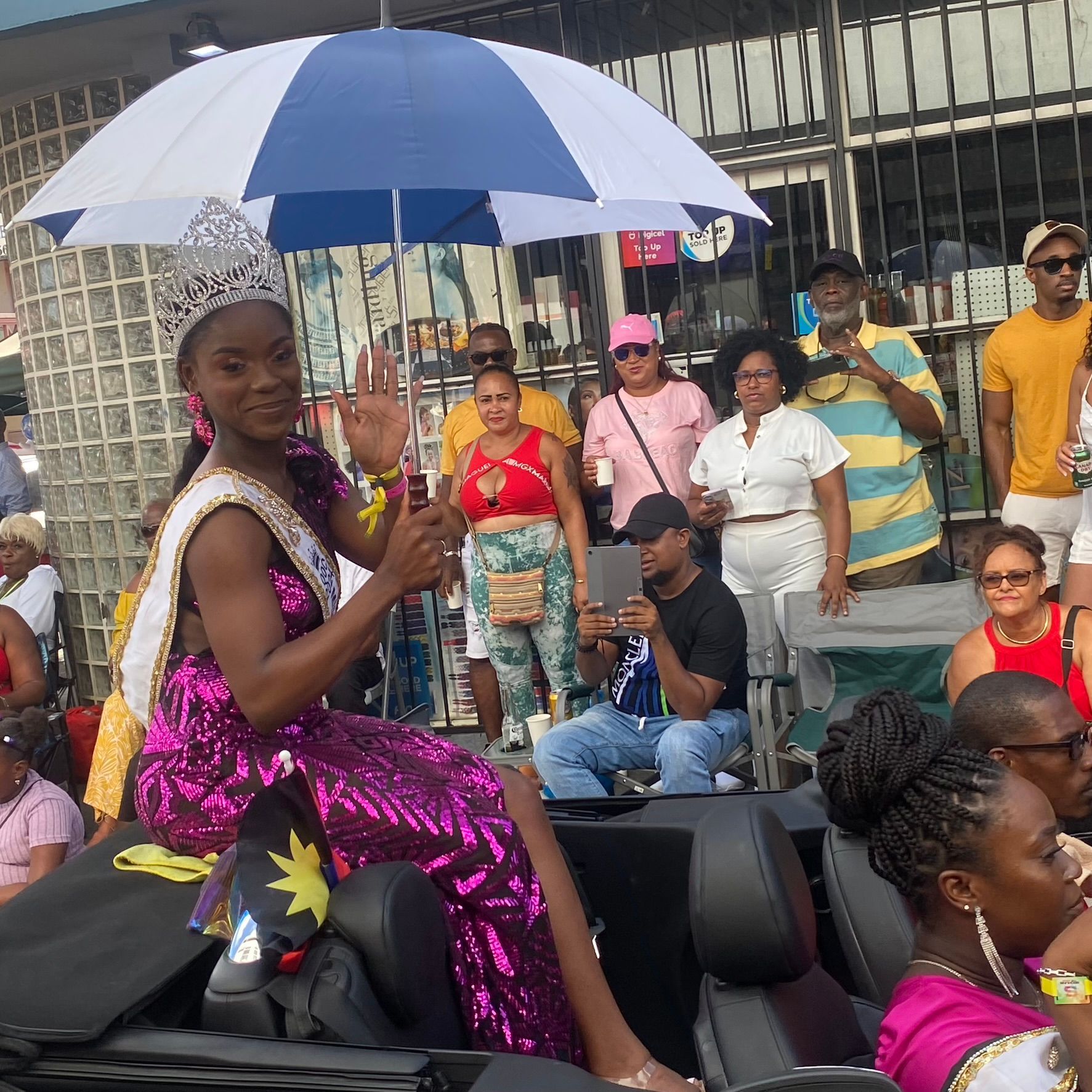 A woman wearing a crown is sitting under an umbrella