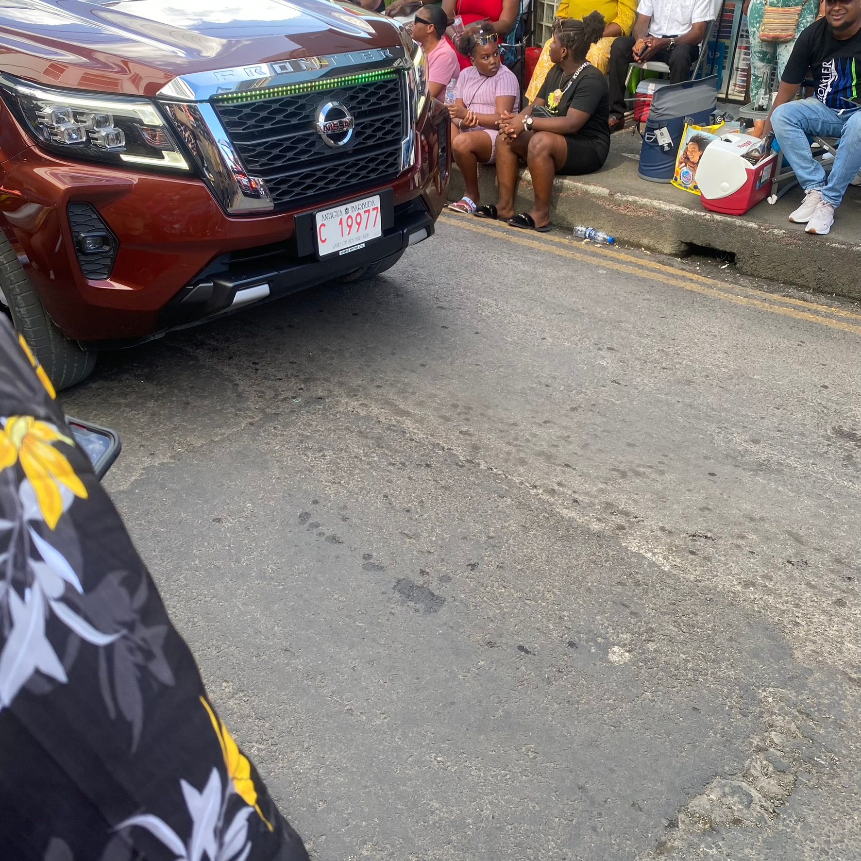 A group of people are sitting on the side of the road next to a car.