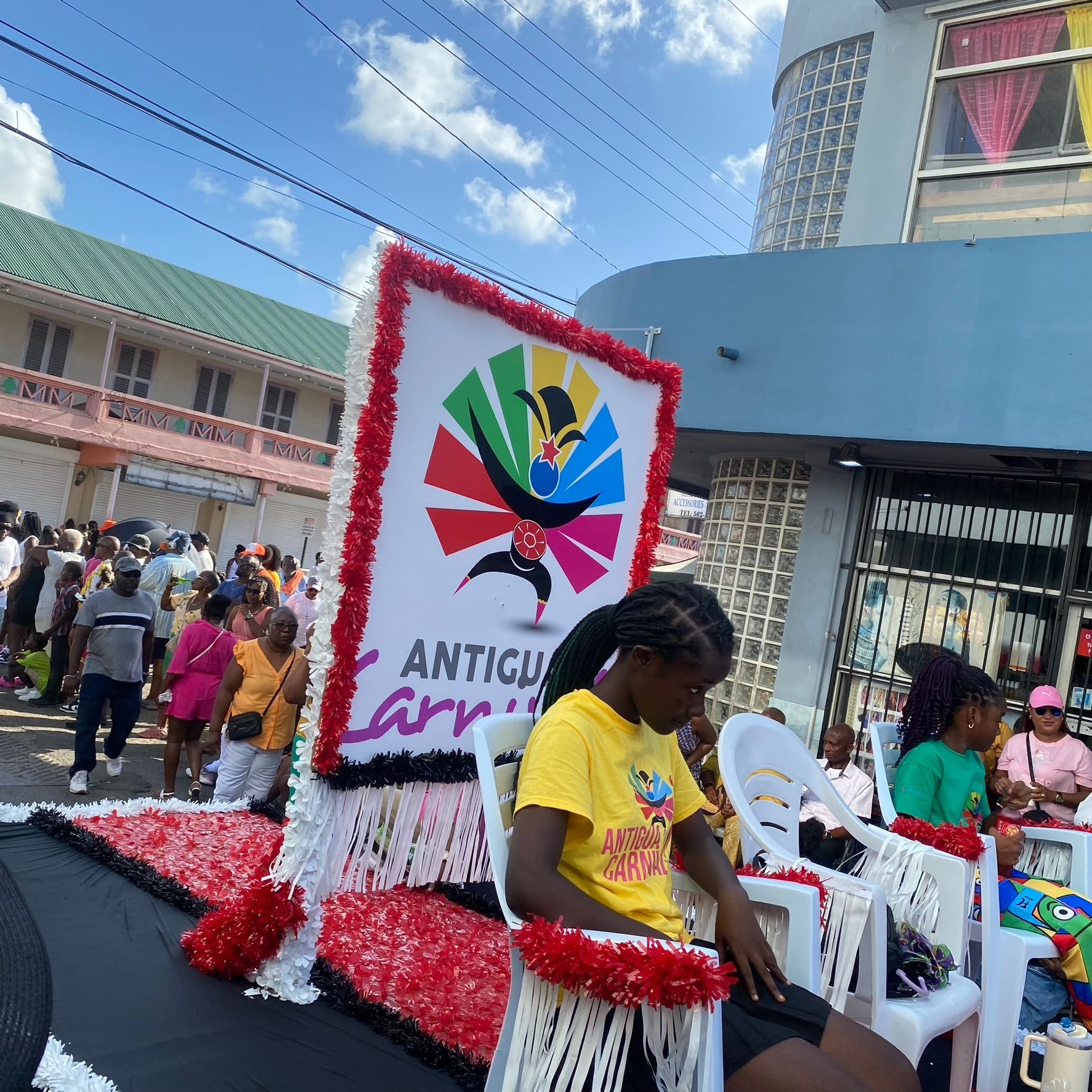 A woman is sitting in a chair in front of a sign that says antigua carnival