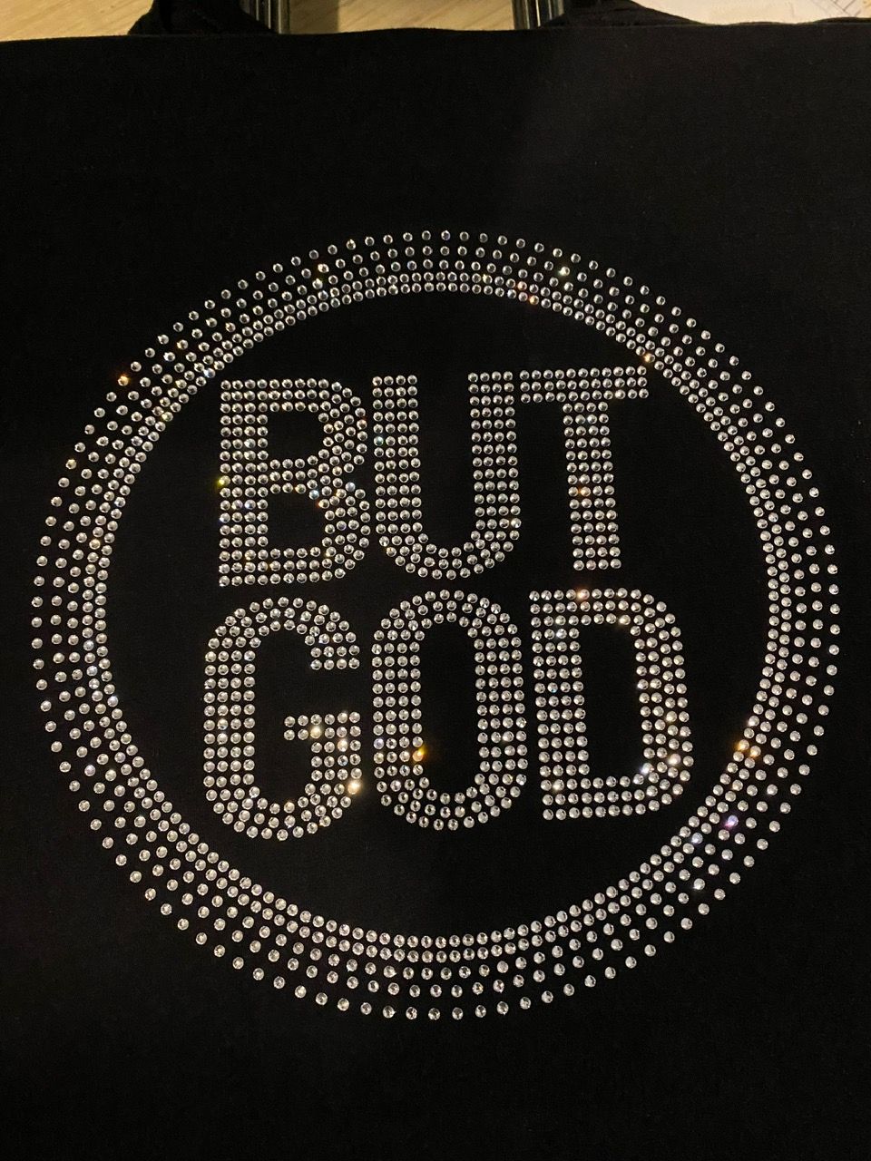 A black shirt with rhinestones that says but god