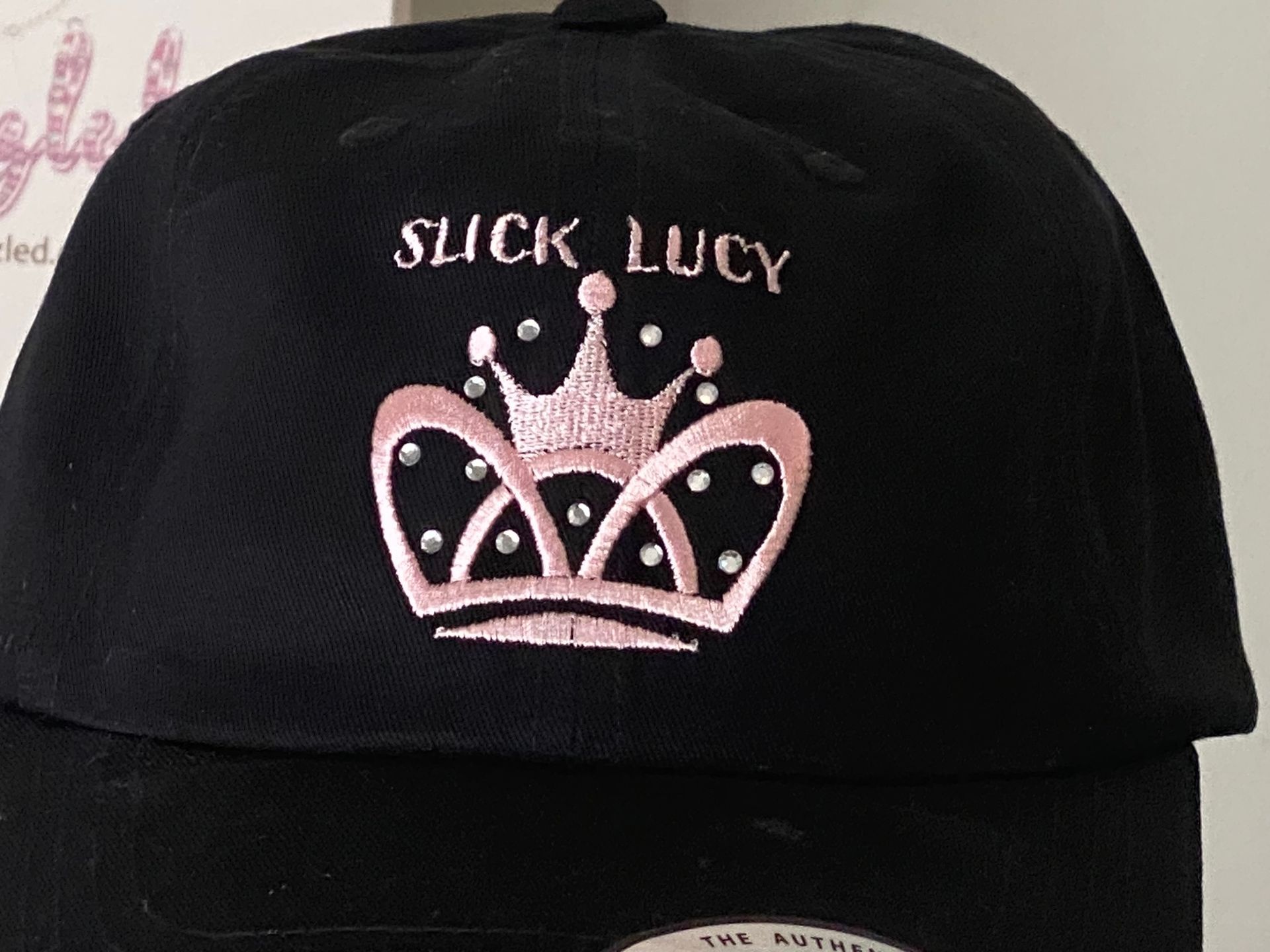 A black hat with a pink crown that says slick lucy