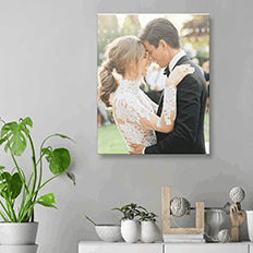 A bride and groom are kissing on a canvas hanging on a wall.