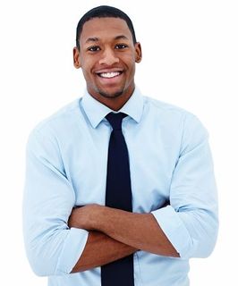 A man in a light blue shirt and black tie is smiling with his arms crossed.