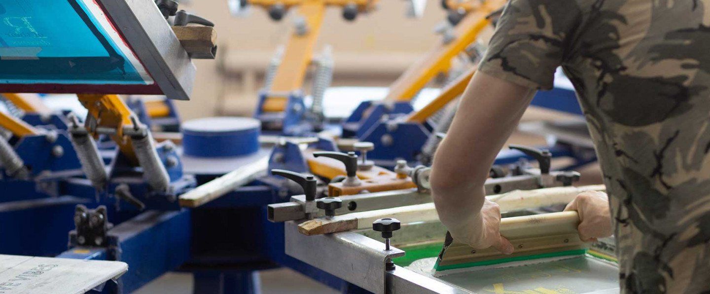 A person is working on a screen printing machine in a factory.