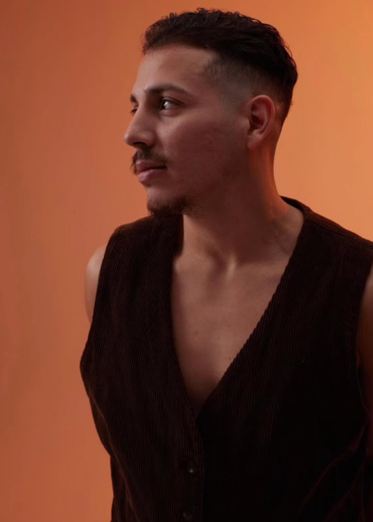 Man in brown vest, looking to the side, against an orange background.