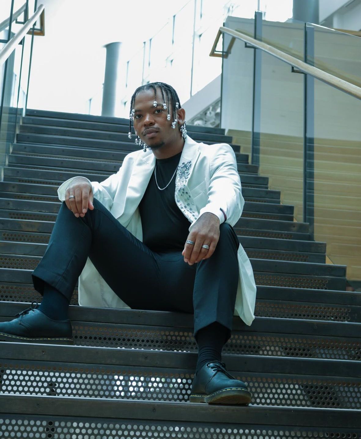 Man in white coat and black pants sits on a staircase, looking at the camera.