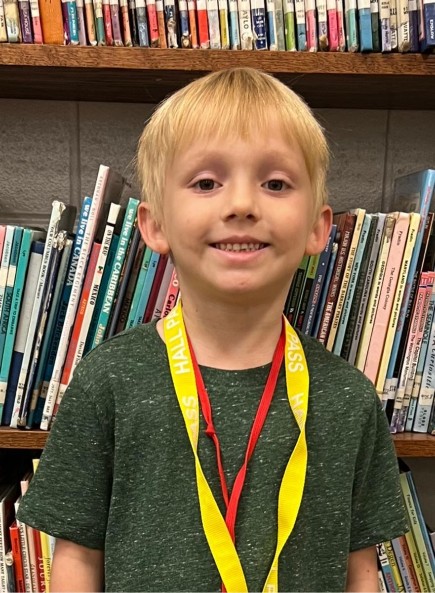 a young boy wearing a medal is standing in front of a bookshelf .