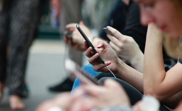 Un grupo de personas están sentadas en fila mirando sus teléfonos móviles.