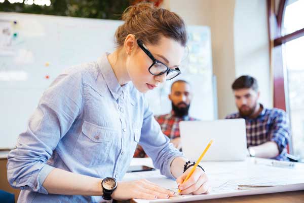 Una mujer está sentada en una mesa escribiendo en una hoja de papel con un lápiz.