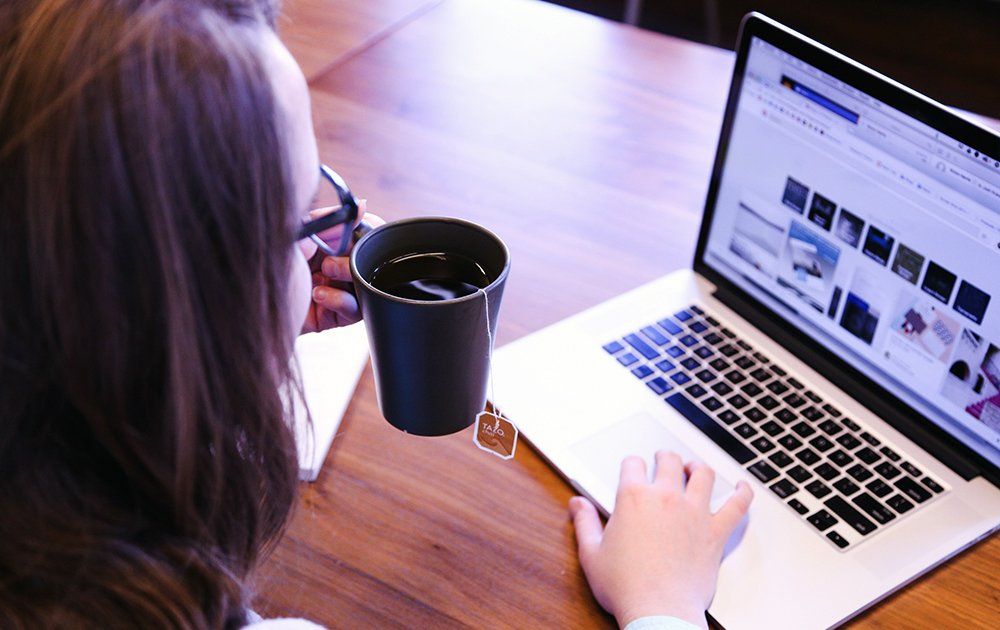 Una mujer está tomando café mientras usa una computadora portátil.