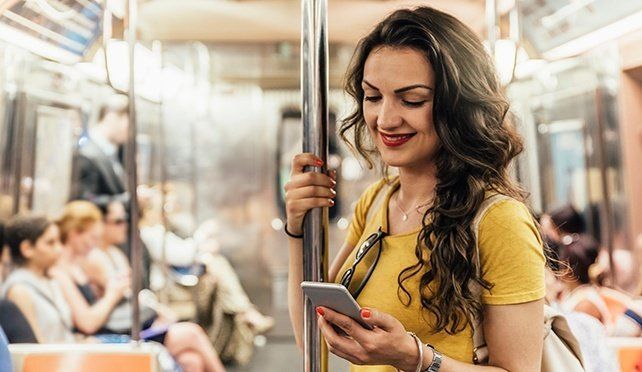 Una mujer está sentada en un tren subterráneo mirando su teléfono celular.
