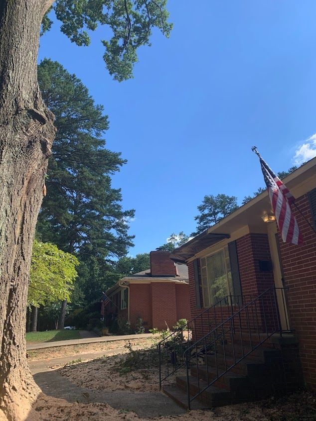 Brick house exterior with an American flag, front steps, and tall trees under a clear blue sky