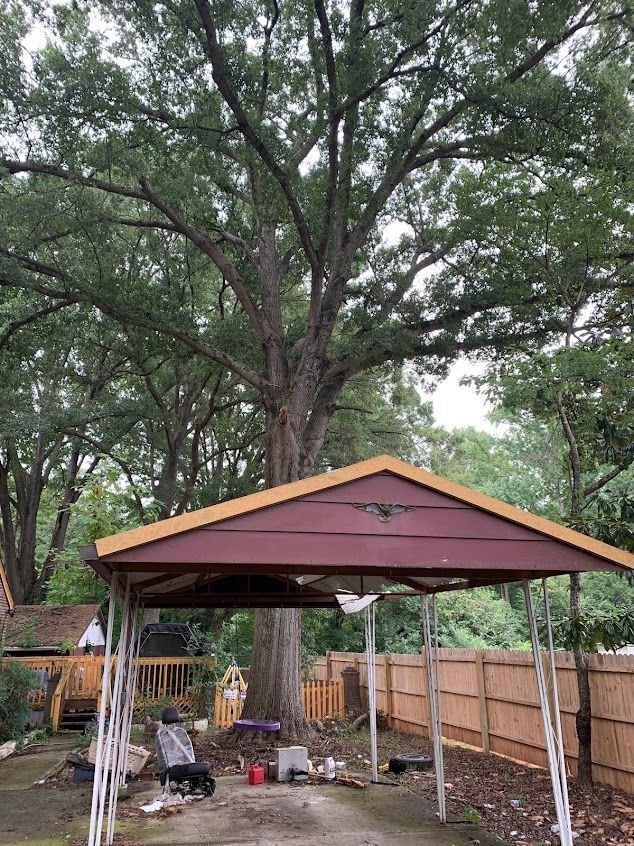 Backyard pavilion with a brown roof and tall trees behind a wooden fence