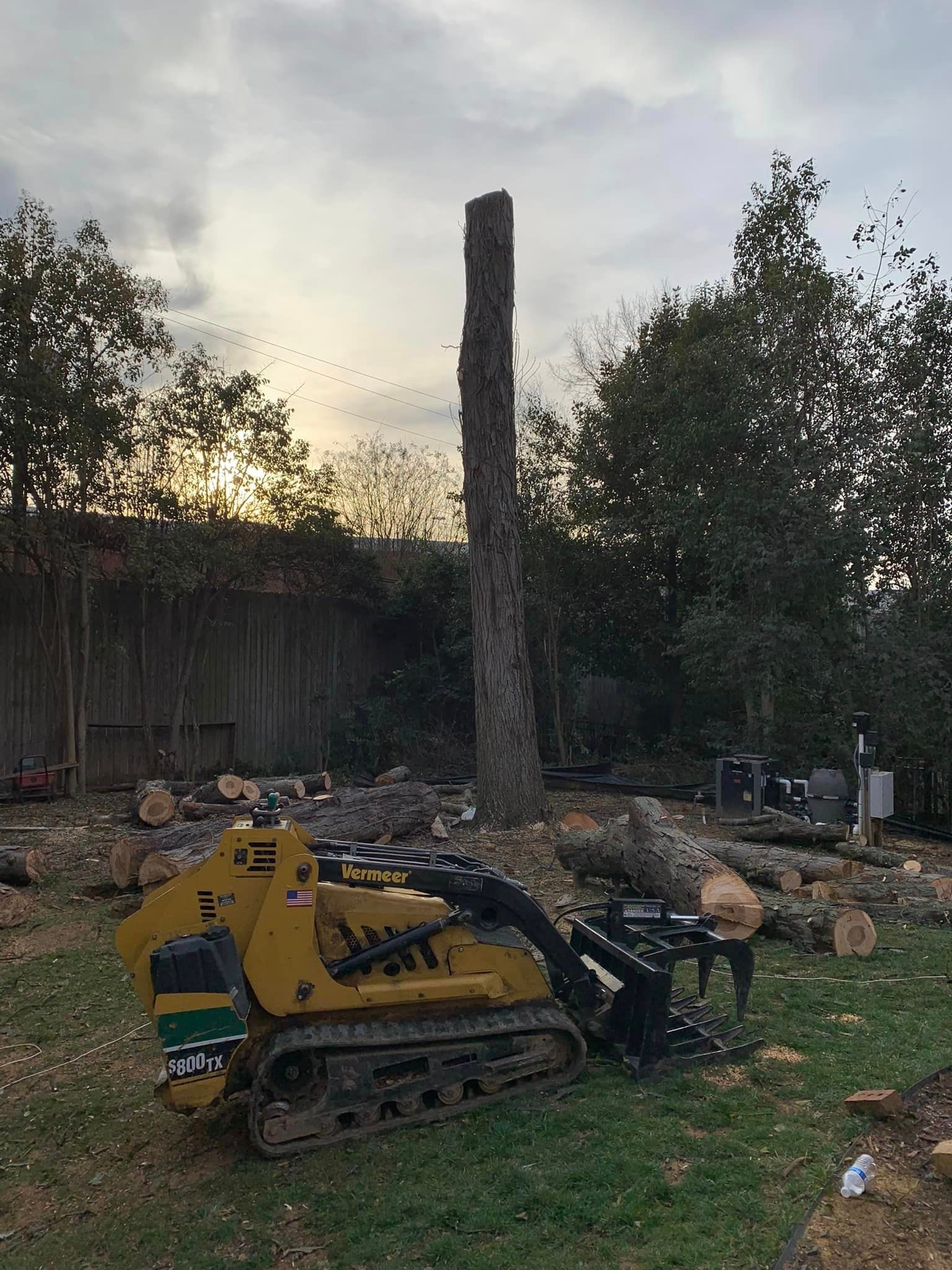 a yellow tractor is sitting in the grass next to a tree stump