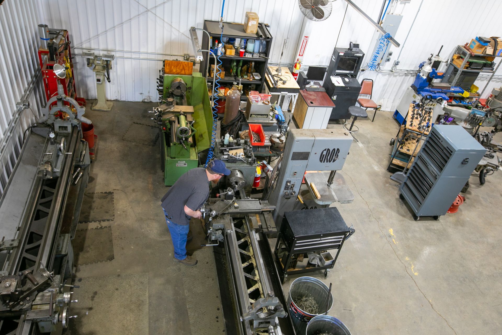 Workshop with industrial machinery, a person inspecting equipment, and workbenches in a concrete-floored shop.