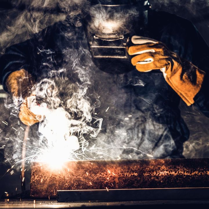 A man is welding a pipe with a welding mask on.