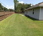 A house with a fence and a lush green lawn in front of it.