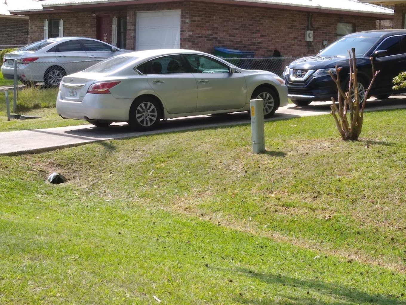 A silver car is parked in front of a brick house.
