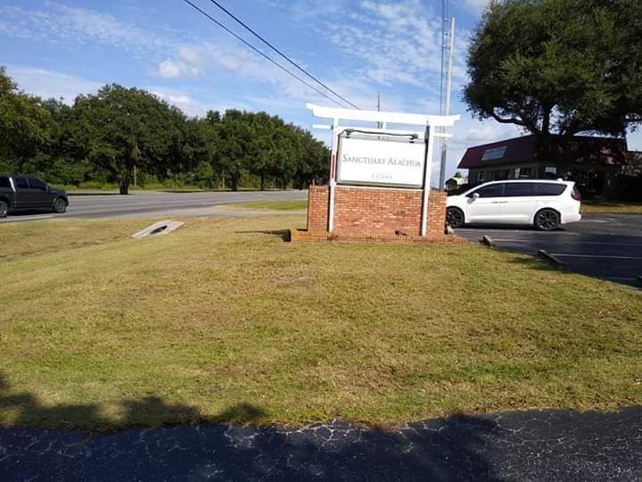 A white van is parked in front of a sign in a grassy field.