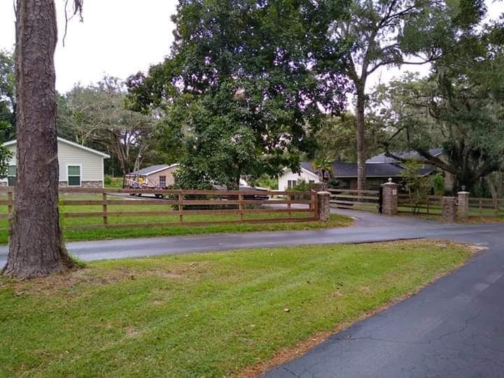A wooden fence surrounds a driveway leading to a house.