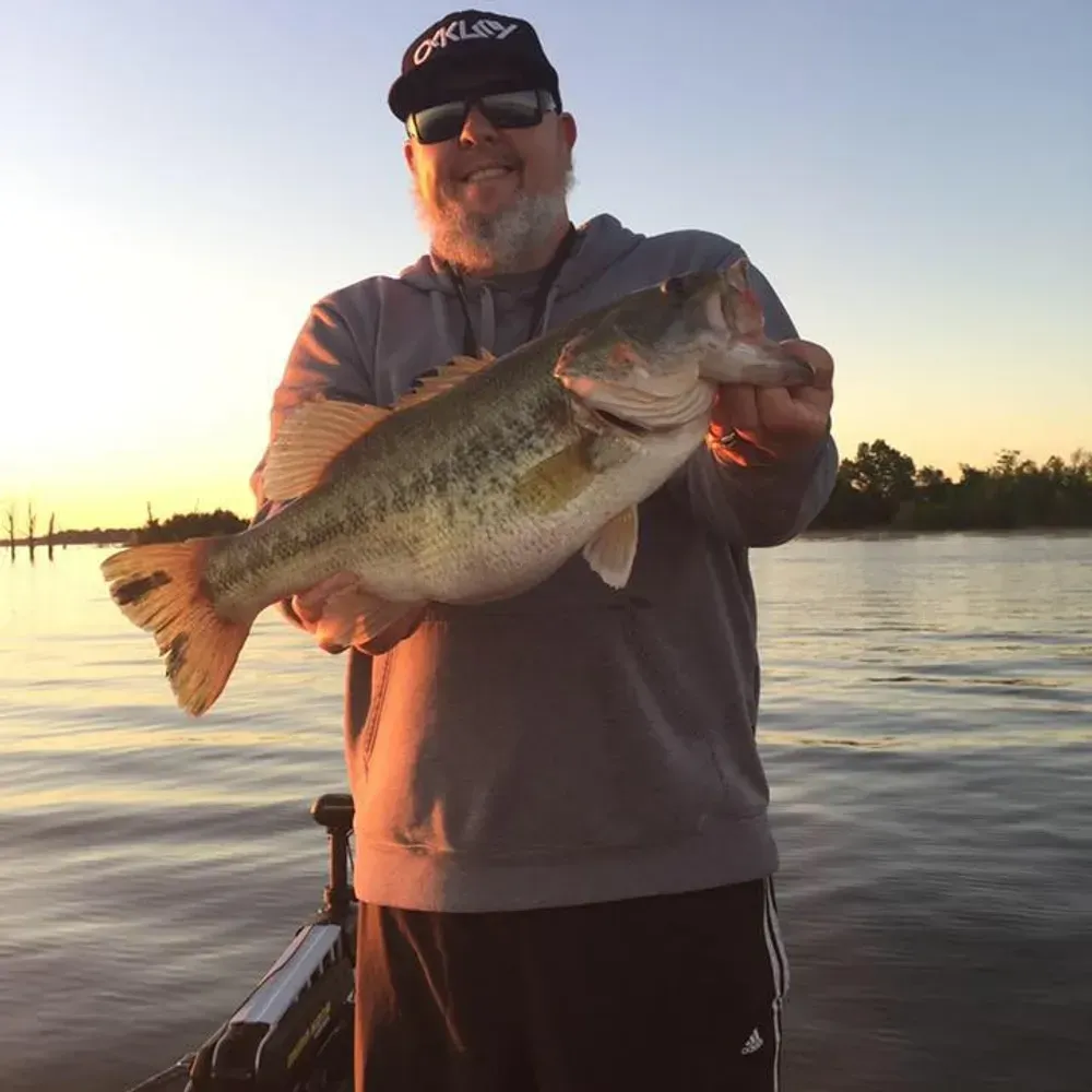 A man wearing an oakley hat is holding a large bass