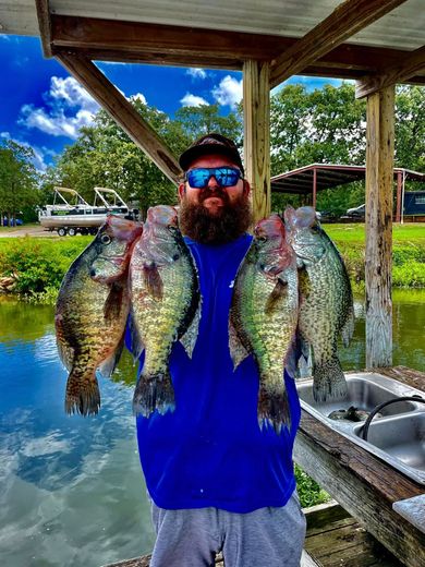 A man with a beard is holding a bunch of fish in front of a lake.