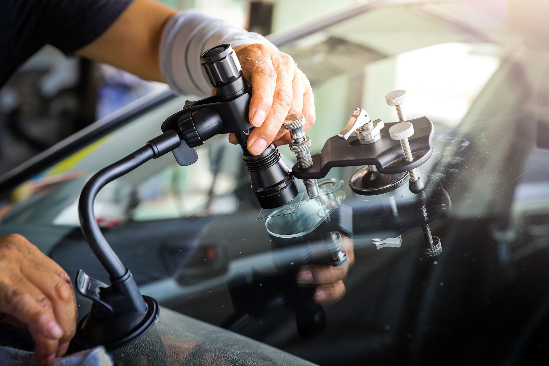A worker is performing a windscreen repair on a broken car glass, using professional equipment.