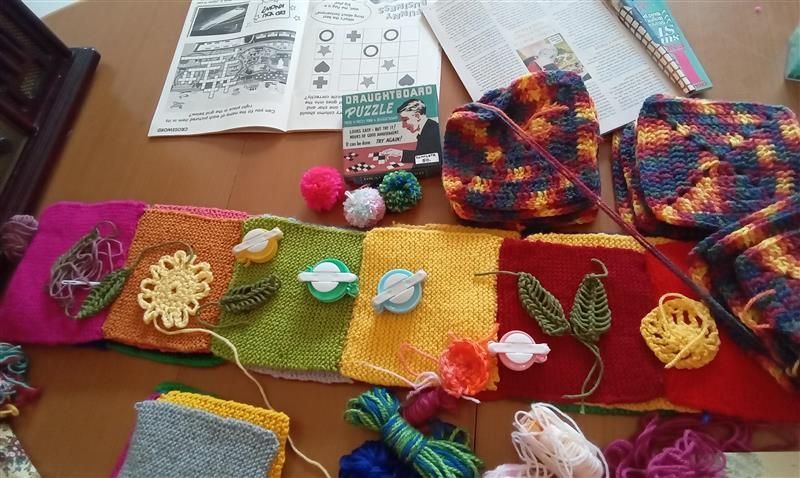 Crocheted squares and accessories in various colors; yarn, patterns, and decorations on a table.