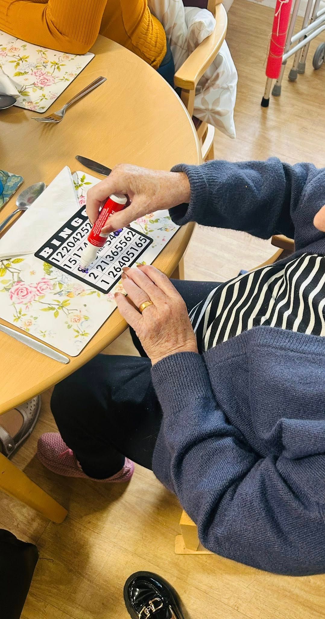 Person marking a bingo card with a red marker at a table, floral tablecloth.