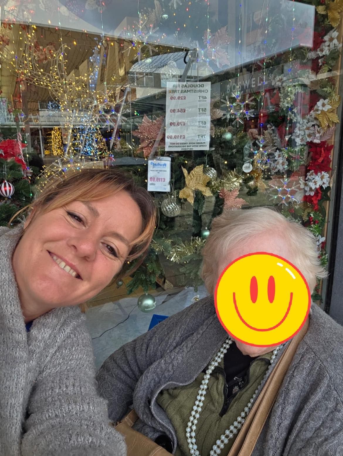 Woman smiling next to a person we support, in front of a store window with Christmas decorations.