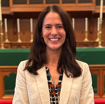 A woman in a white jacket is smiling in front of a church altar.