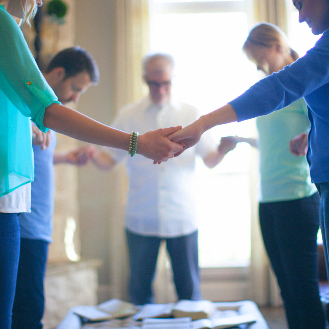 A group of people are holding hands in a circle in a living room.