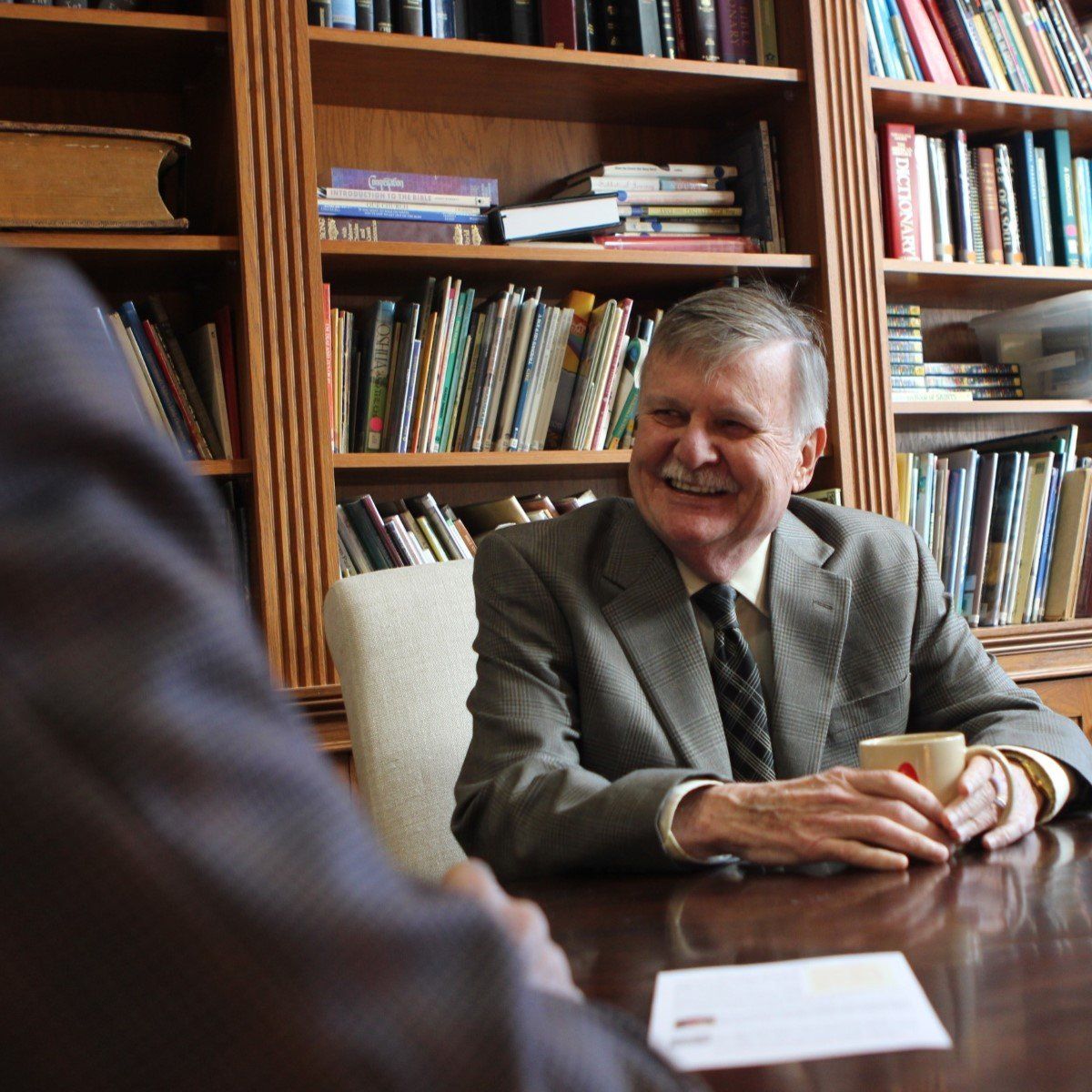 A man in a suit and tie is sitting at a table with a cup of coffee