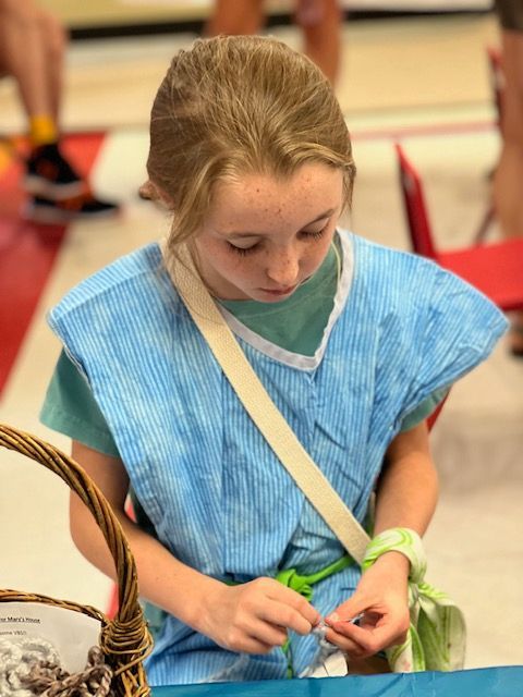 A young girl in a blue dress is sitting at a table with a basket.