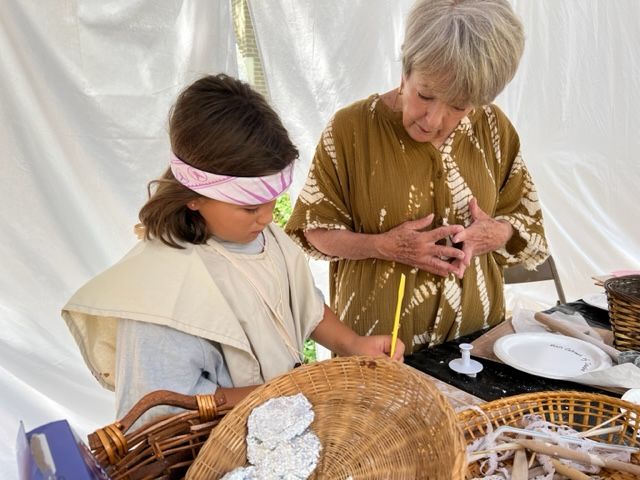 A woman and a child are sitting at a table with baskets and plates.