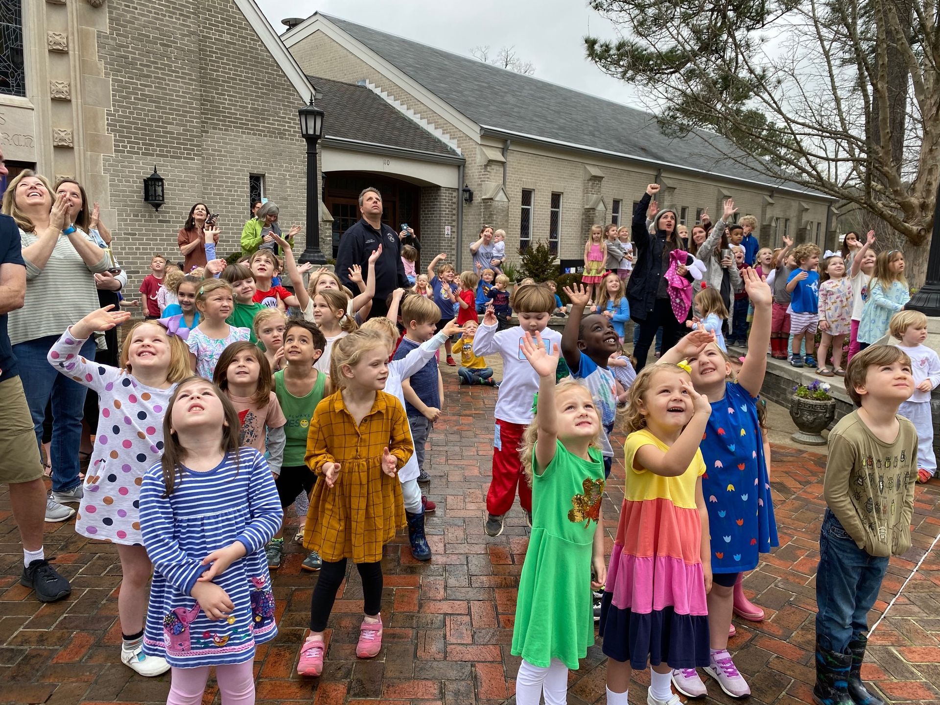 A group of children are standing in front of a church with their hands in the air.
