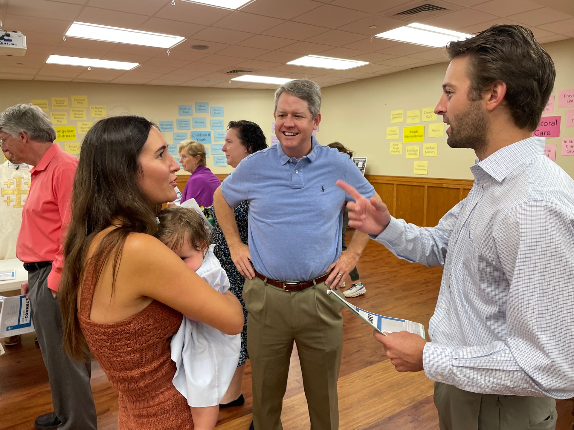 A woman is holding a baby while talking to two men in a room.