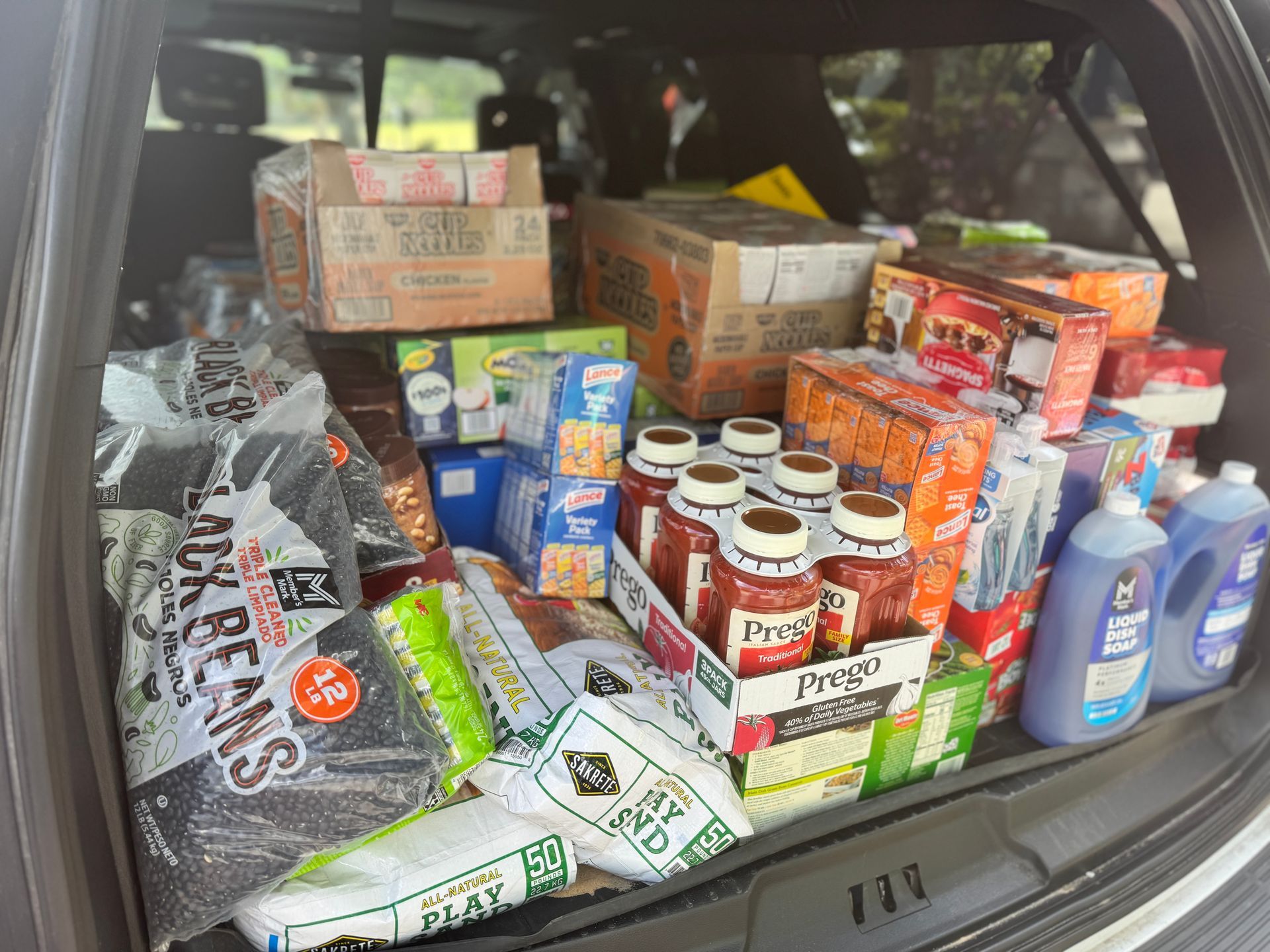 The back of a car is filled with lots of food and cleaning supplies.