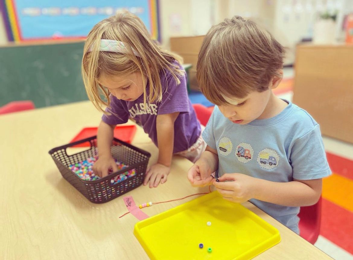 A boy and a girl are sitting at a table playing with beads.