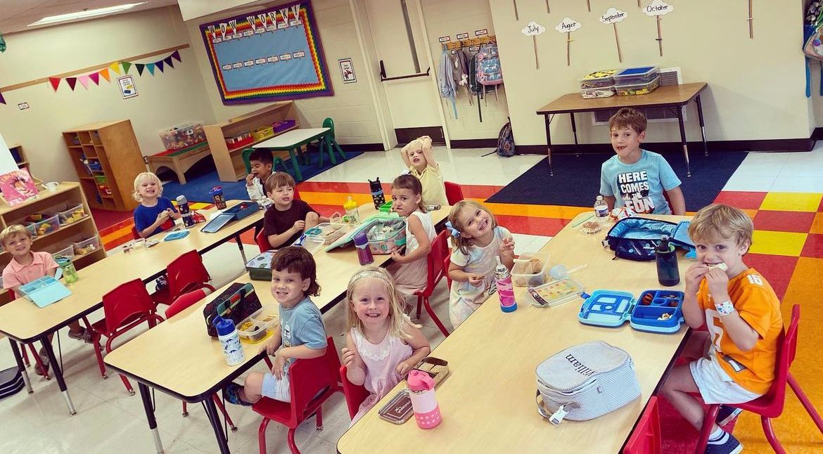 A group of children are sitting at tables in a classroom.