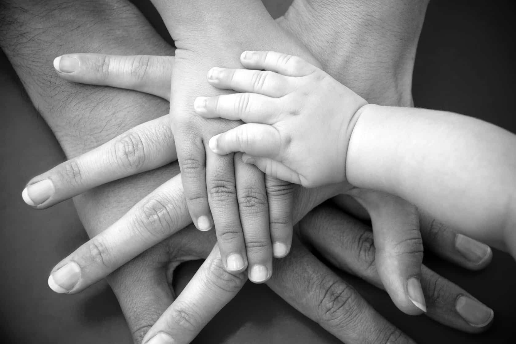 A black and white photo of a family putting their hands together