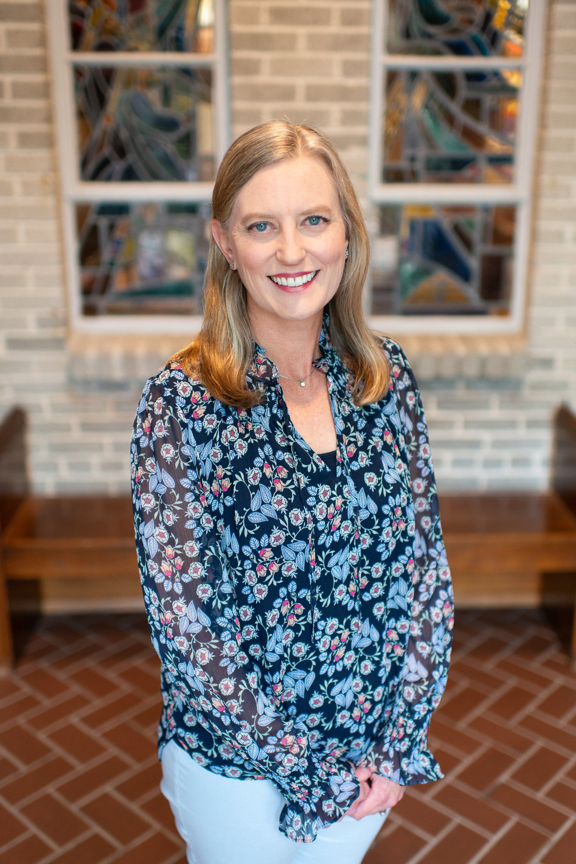 A woman in a floral shirt is standing in front of a stained glass window.