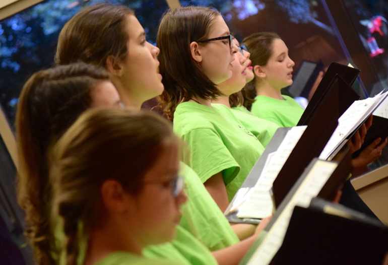 A group of young girls in green shirts are singing in a choir.