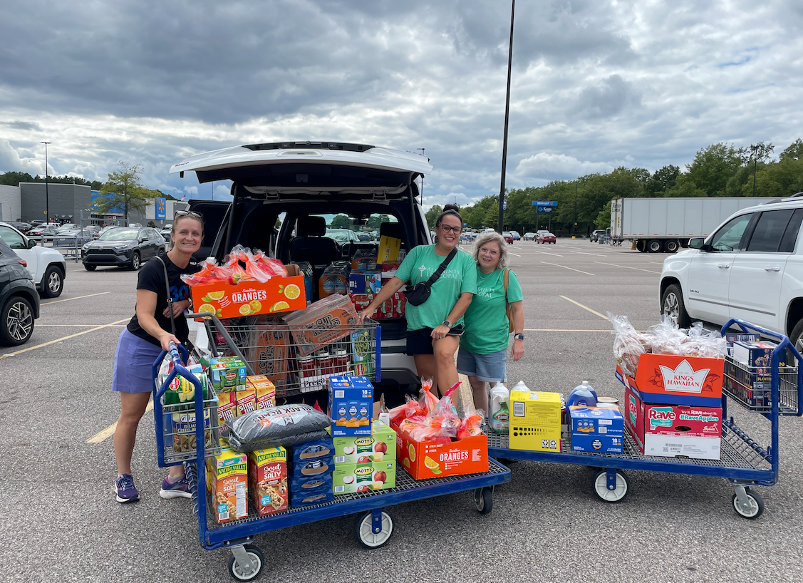 A group of women are standing next to carts filled with groceries in a parking lot.