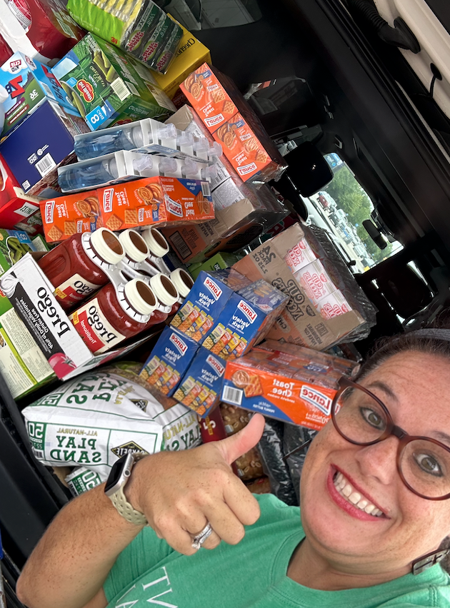 A woman is giving a thumbs up in front of a pile of food.