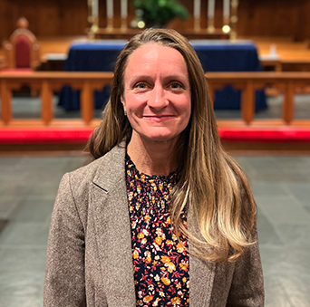 A woman is standing in front of an altar in a church and smiling.